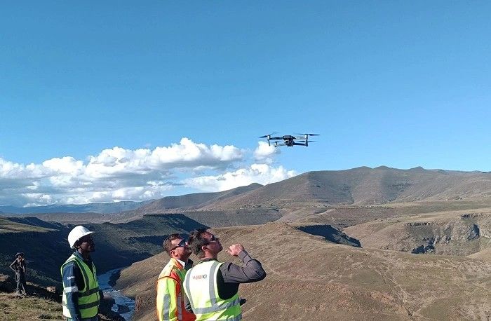 Three surveyors flying a drone above a valley