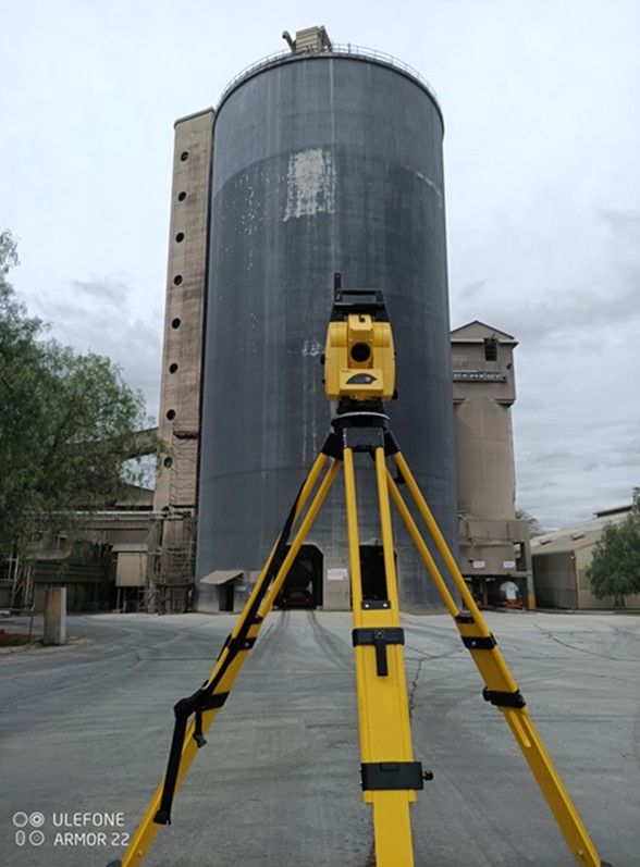 A total station set up in front of a concrete silo