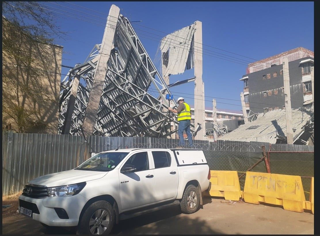 A surveyor on a collapsed concrete structure, with a bakkie in front