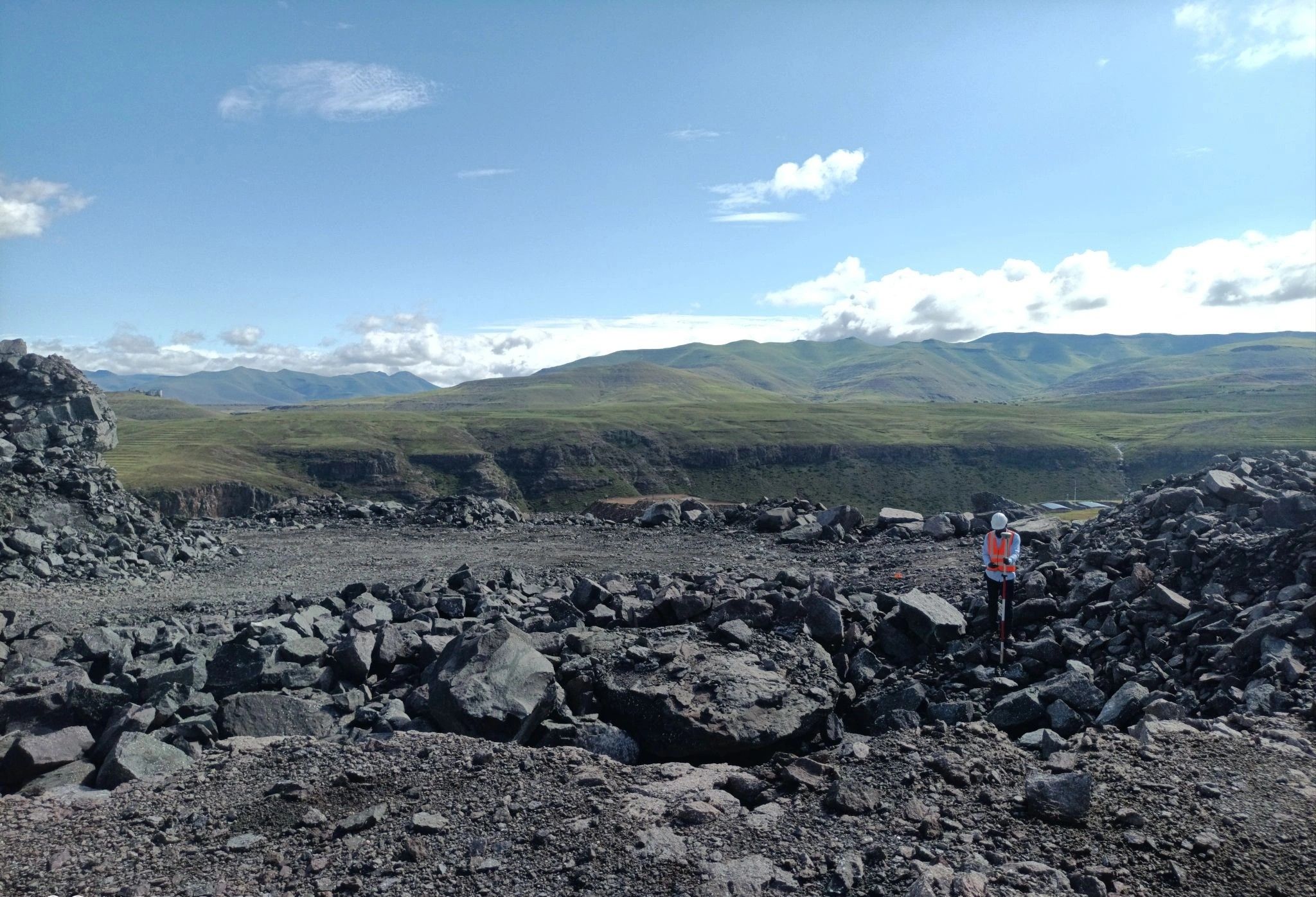 An open-pit mine under a wide sky, with a surveyor on the far bench
