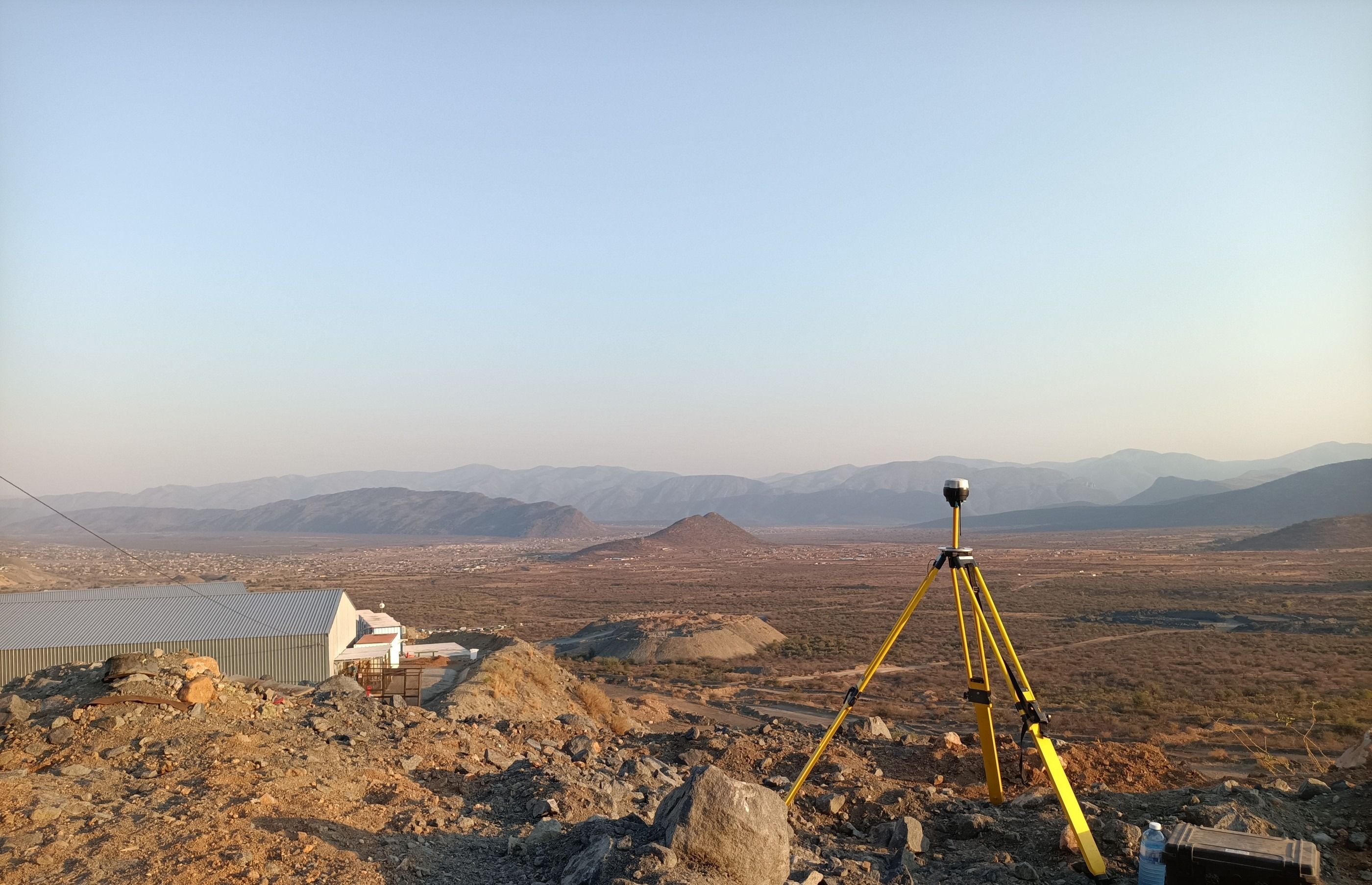 A GNSS receiver on a tripod above a mine site at sunrise