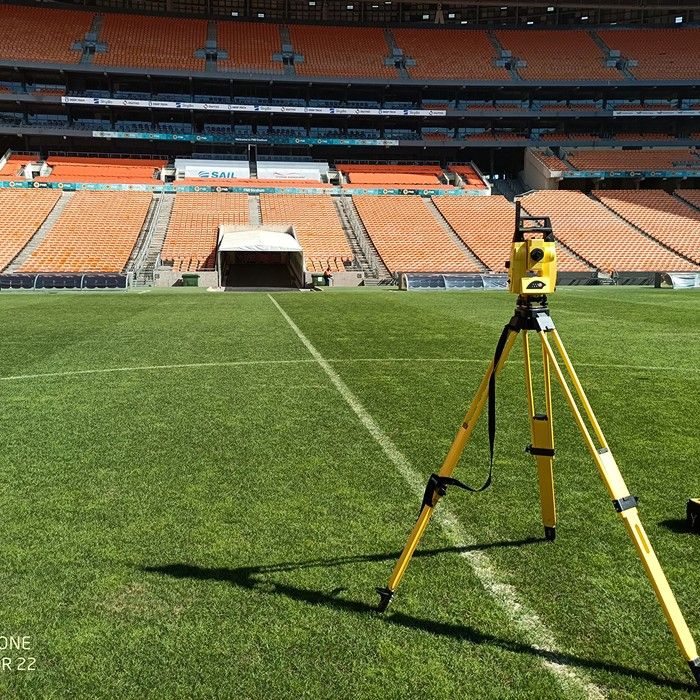 A total station on the pitch in front of the orange stands