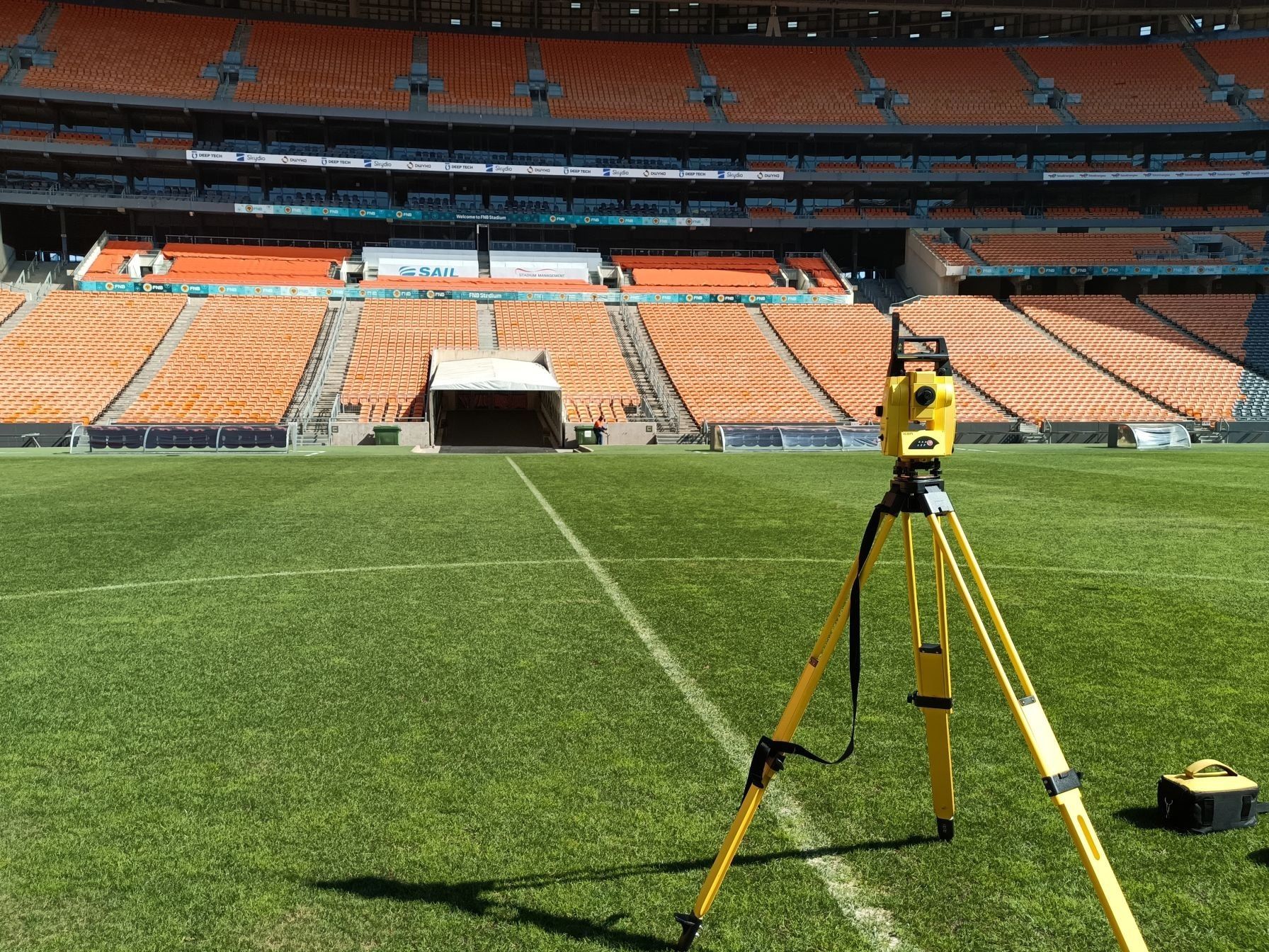 A total station on a yellow tripod on the pitch at FNB Stadium