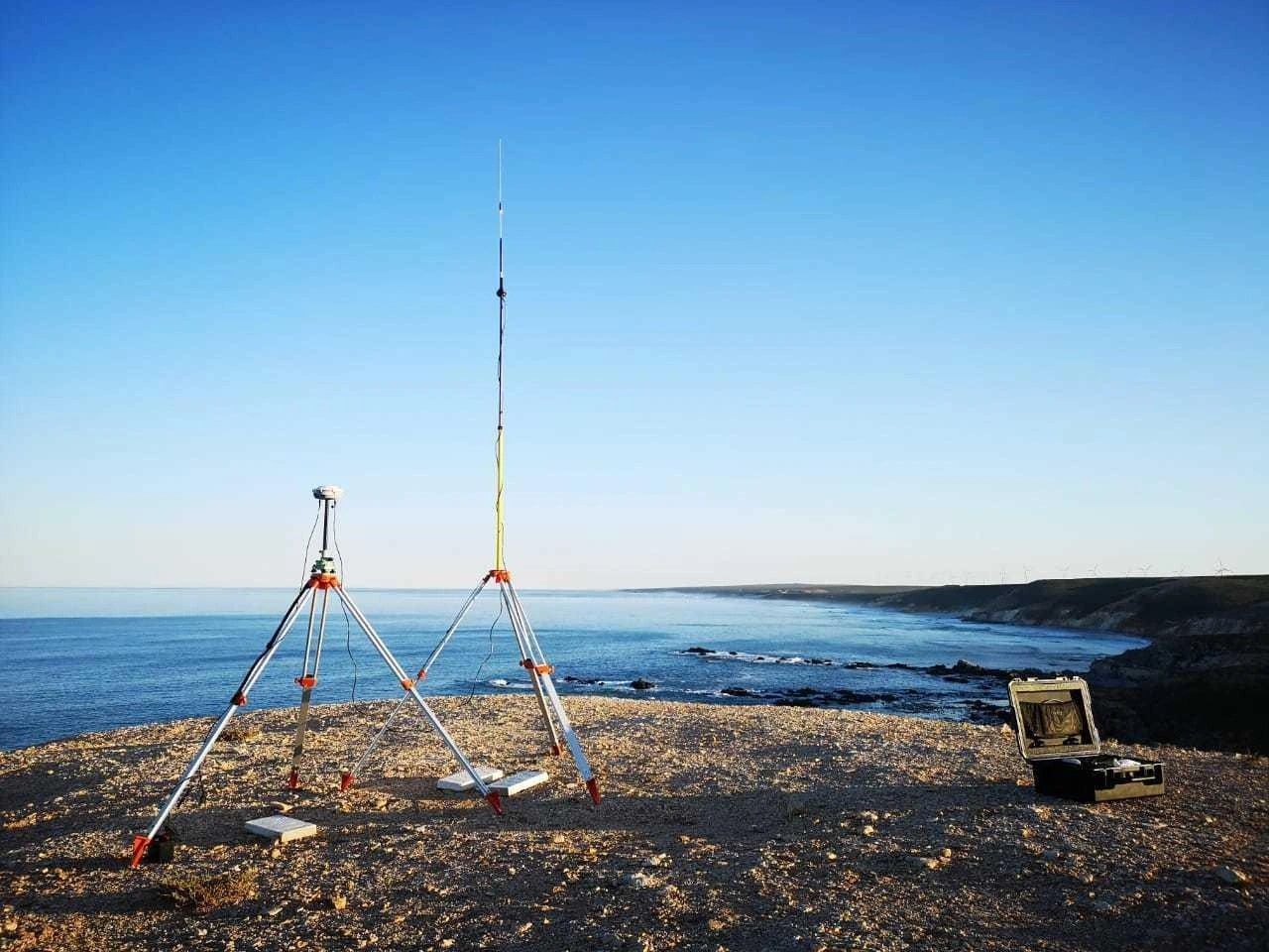 A GNSS base station on a tripod set up above the coastline