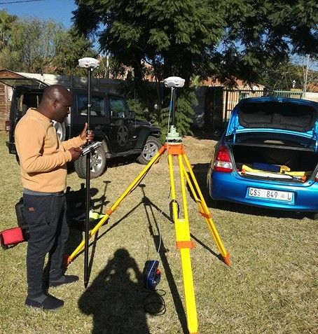 A surveyor with a GNSS receiver and tripod, working next to parked vehicles