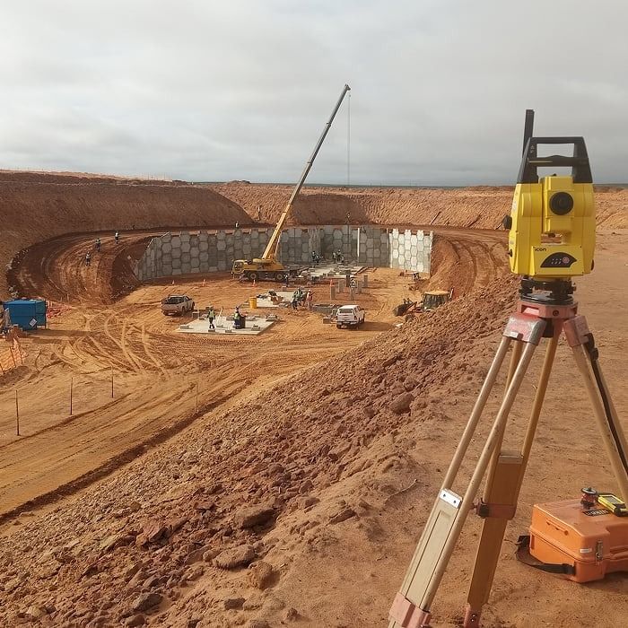 A total station overlooking an excavation with a crane and the precast wall