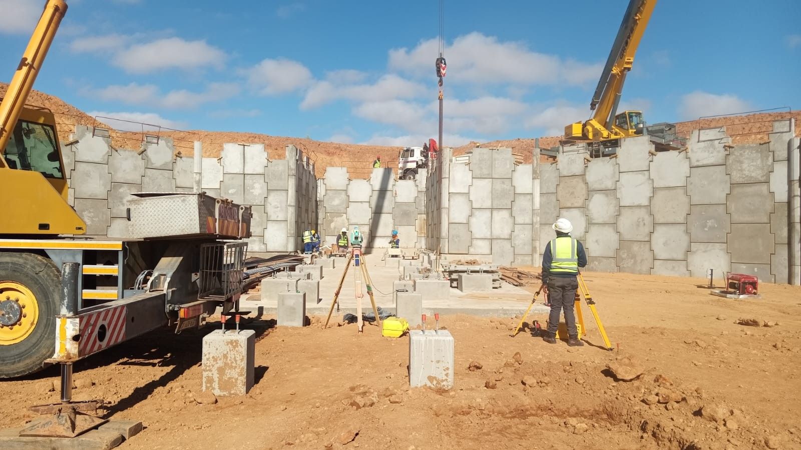 A precast concrete wall being assembled with a mobile crane on red soil