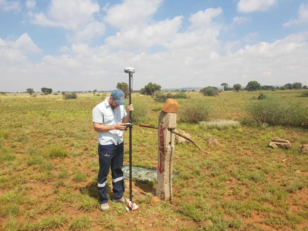 A surveyor with a GNSS pole at a fence corner post in open veld