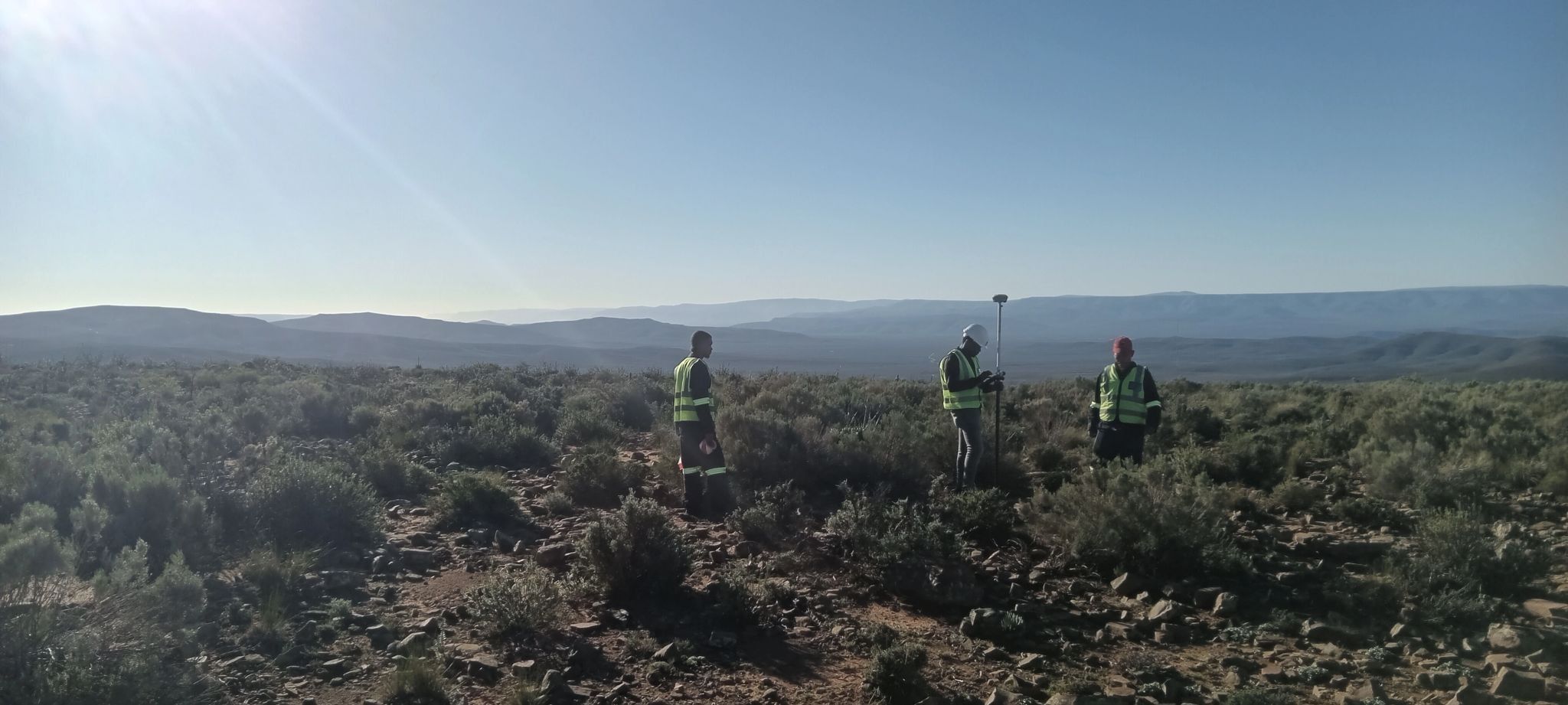 Three surveyors in hi-vis vests in scrubland
