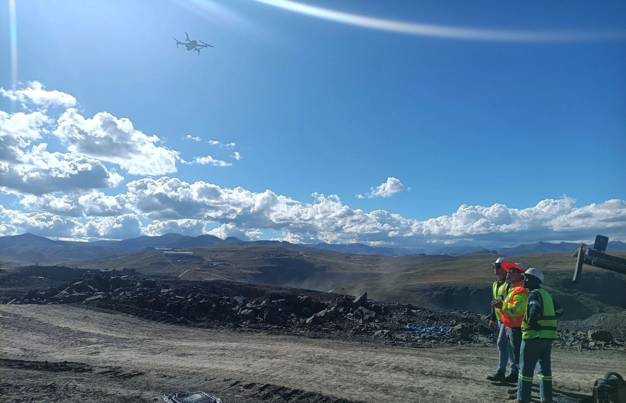 Two surveyors at the edge of an open-pit mine with a drone in the air