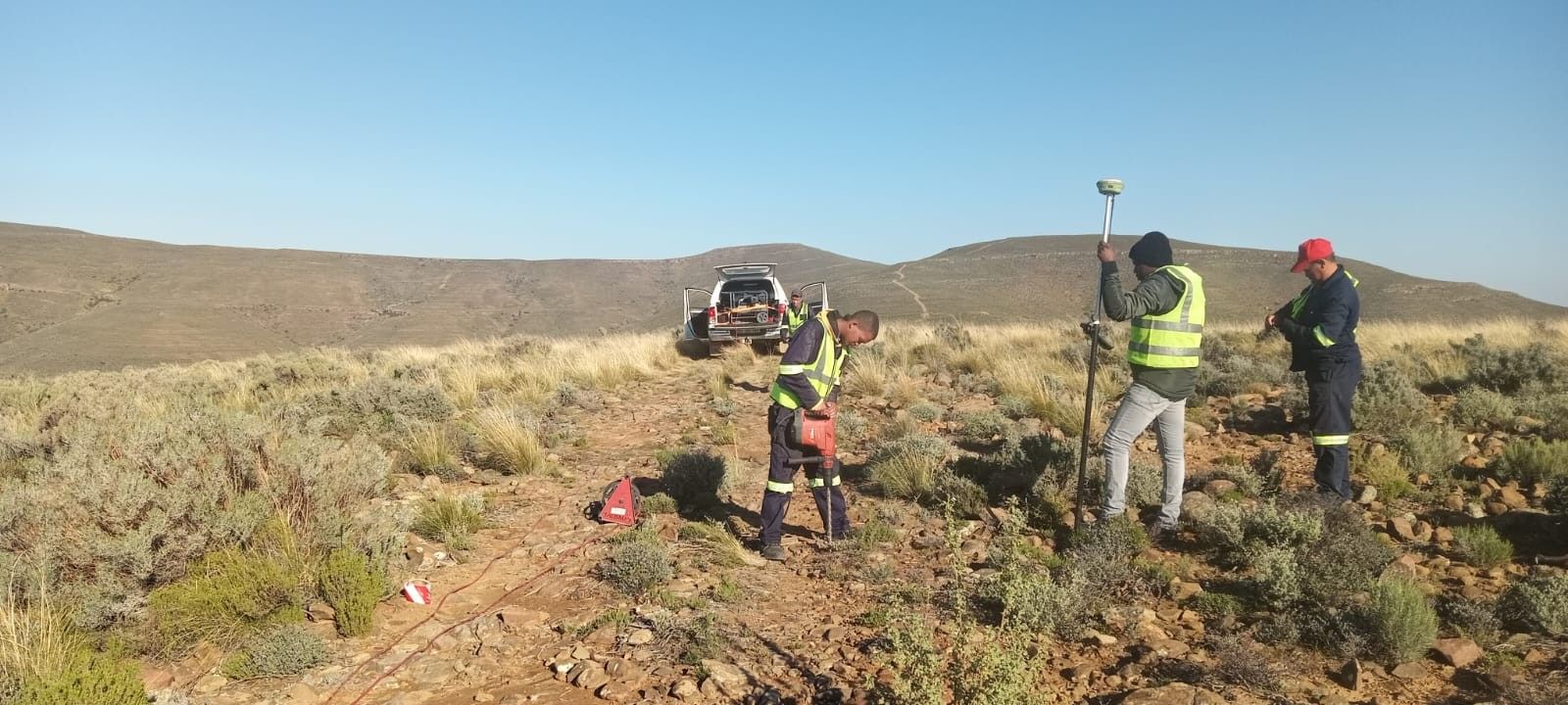 Surveyors with a GNSS pole and a bakkie in the veld at the Oya site