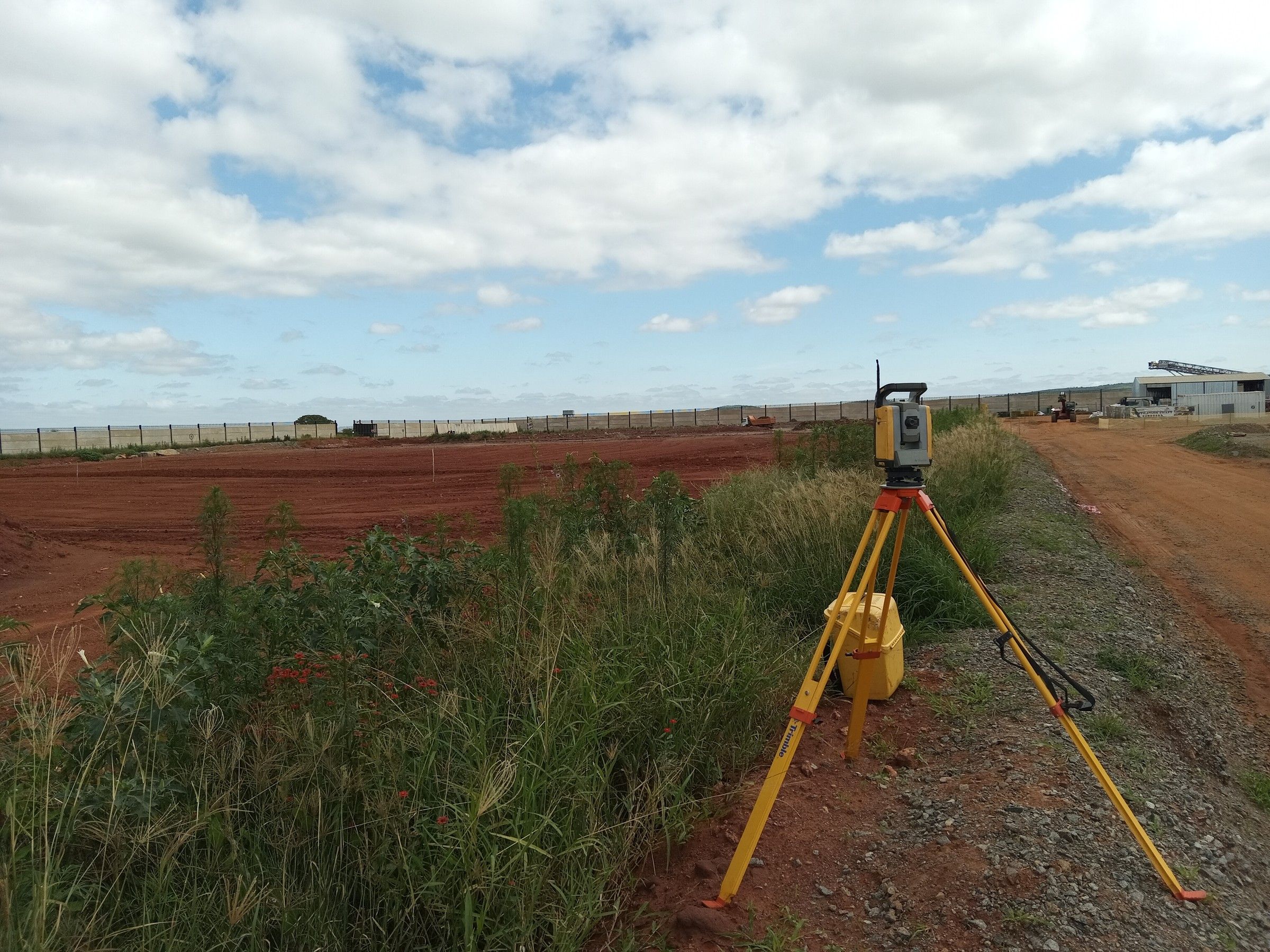 A total station on a tripod next to a red-soil field