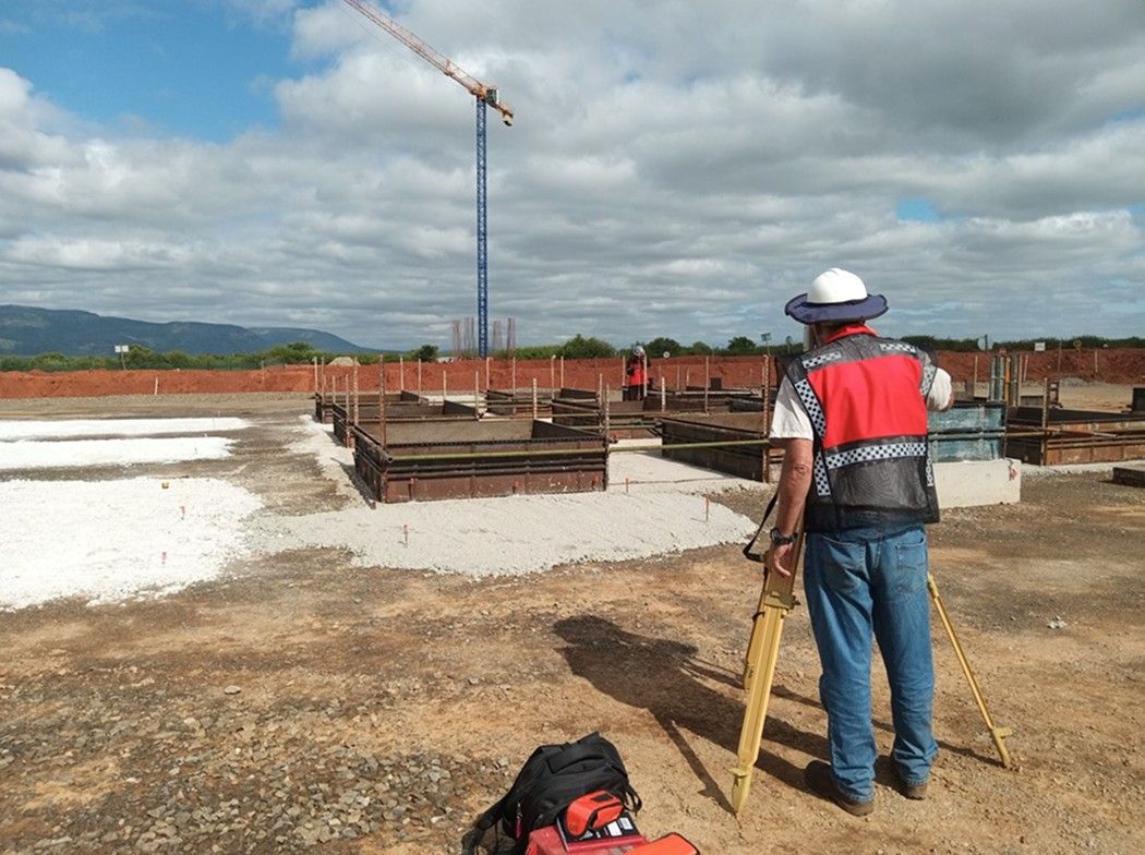 A surveyor with a GNSS pole beside a construction pad, with a crane in the distance