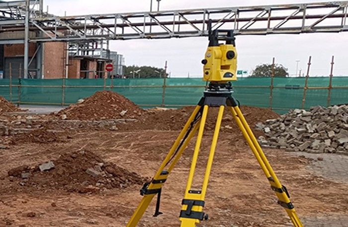 A total station on a yellow tripod at a construction site